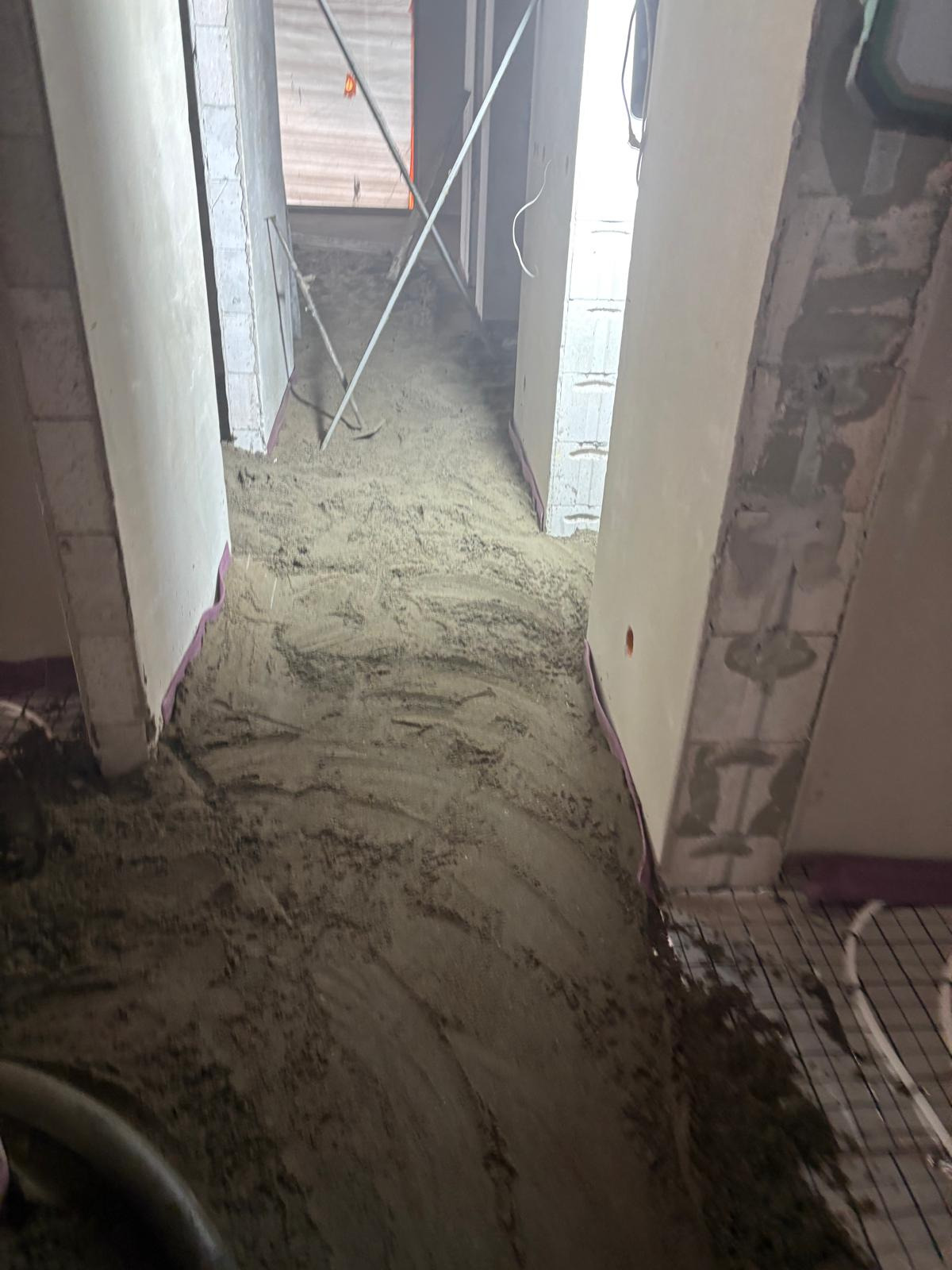 Wnętrze w trakcie wylewki posadzki maszynowej z widocznym ogrzewaniem podłogowym i narzędziami. Ściany surowe, przygotowane do dalszych prac wykończeniowych.