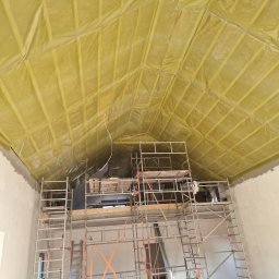Marbud - Skośny sufit poddasza z izolacją z folii i wełny mineralnej, widoczny ze stojącego rusztowania. Ściany w surowym tynku.