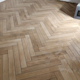 Gut-pro usługi remontowe - Ukończona podłoga z płytek imitujących drewno, ułożonych w jodełkę, w rogu pomieszczenia z widocznymi gniazdkami elektrycznymi i fragmentem grzejnika.