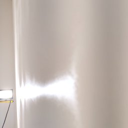 Gut-pro usługi remontowe - Świeżo pomalowana, gładka ściana w jasnym odcieniu bieli, oświetlona lampą budowlaną, ukazująca precyzję wykonania i brak niedoskonałości. Widoczne ślady po wałku.