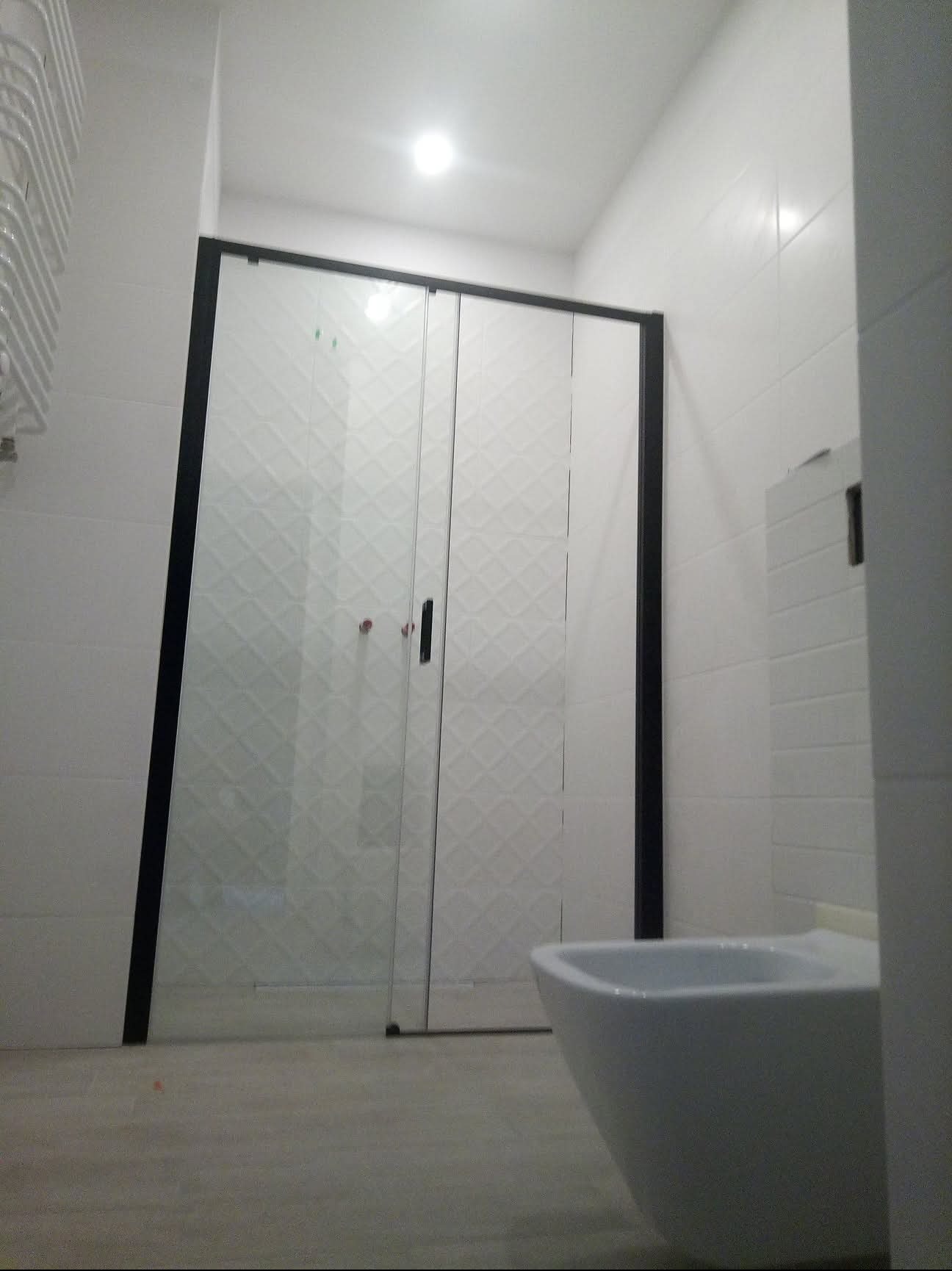 Nowoczesna kabina prysznicowa z czarną ramą i wzorem na szkle, biała ceramika łazienkowa, jasne płytki. Minimalistyczny design łazienki po remoncie.