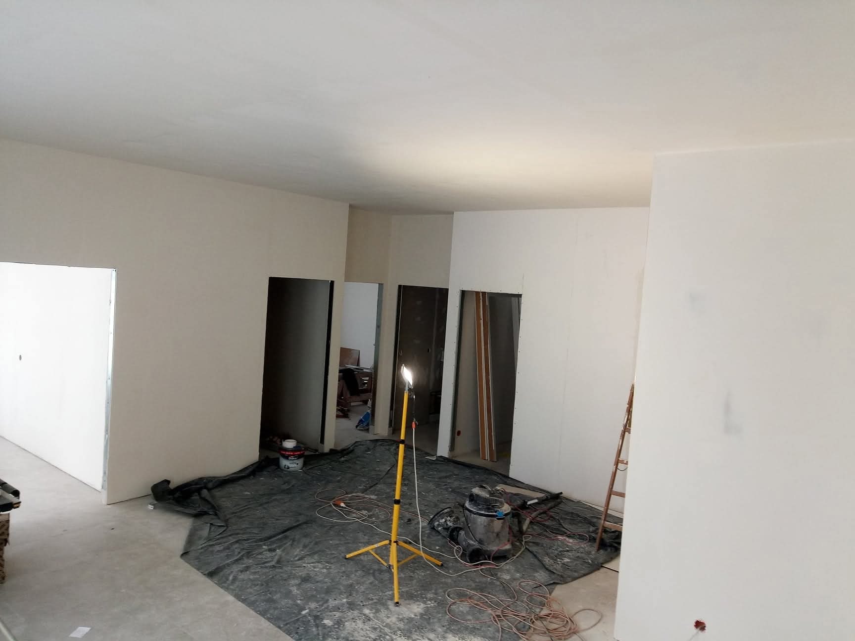 Wnętrze w trakcie prac wykończeniowych: świeżo pomalowane ściany, widoczne narzędzia, lampa oświetlająca przestrzeń, przygotowane do dalszych etapów prac.