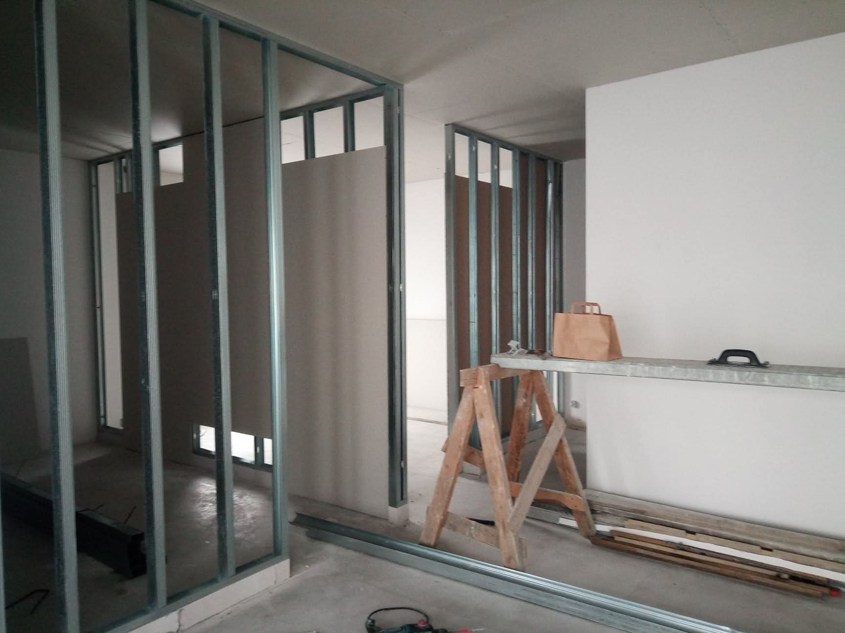 Montaż ścianki działowej z płyty karton-gips na metalowym stelażu. Widoczne narzędzia i materiały budowlane. Surowy stan wykończenia wnętrza.