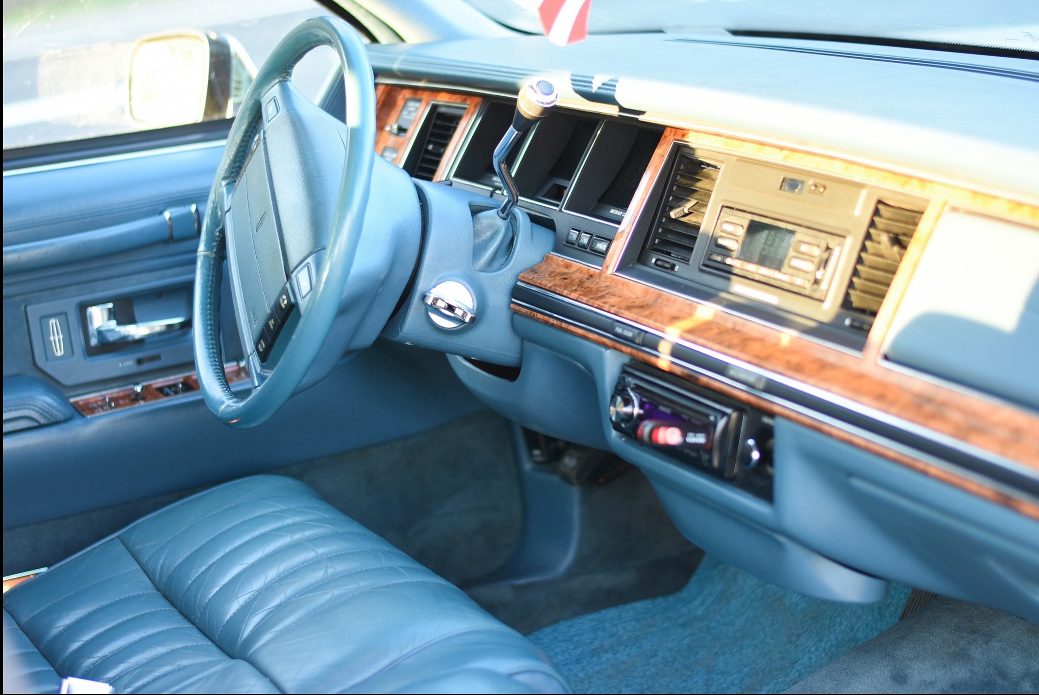 Wnętrze klasycznego, błękitnego samochodu z drewnianymi akcentami. Widoczna kierownica, deska rozdzielcza i skórzane siedzenia. Detale retro i dbałość o szczegóły.