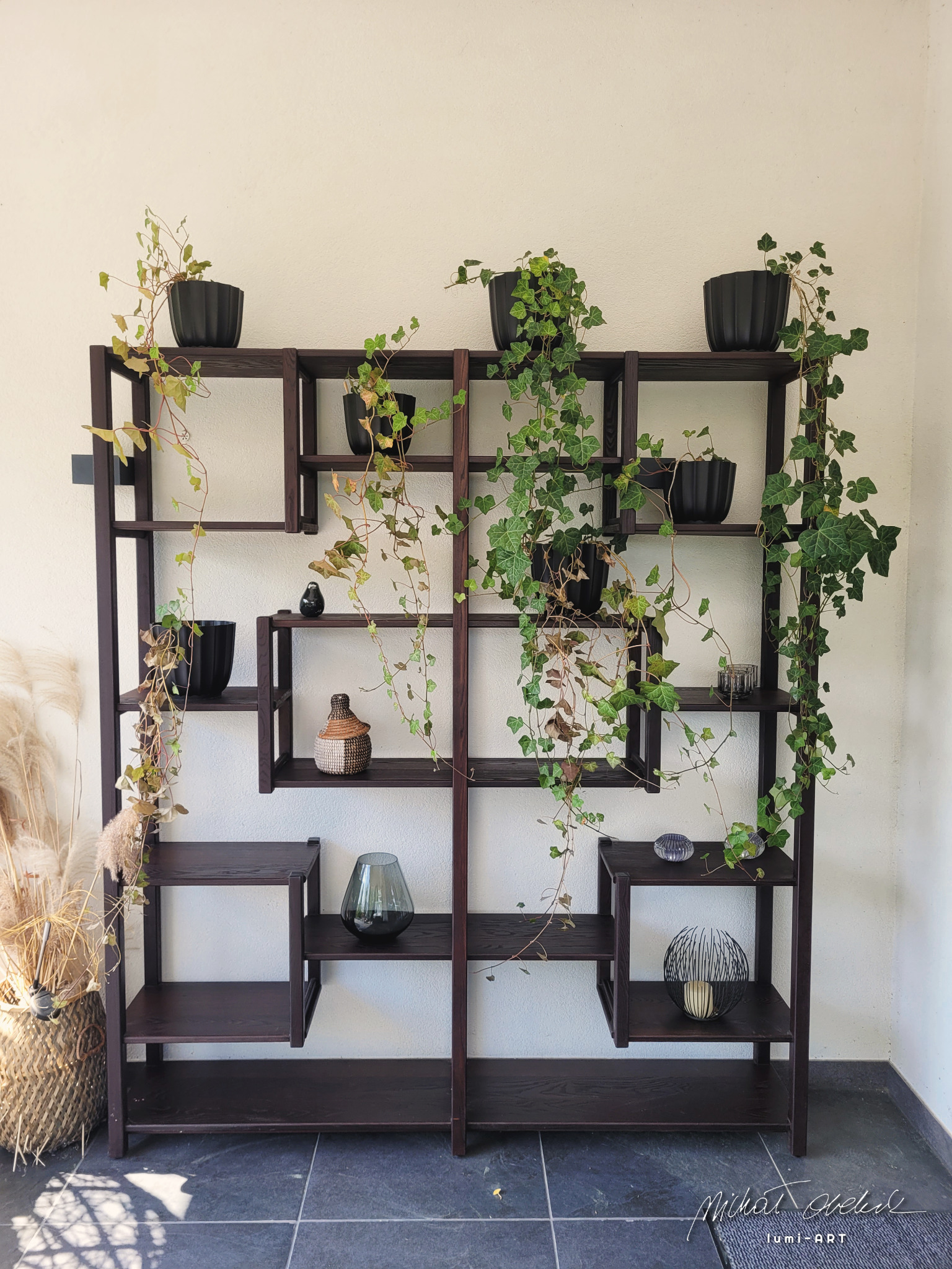 Ręcznie robiony regał z ciemnego drewna, zdobiony roślinami doniczkowymi i dekoracjami, w nowoczesnym stylu, wykonany w Kielcach. Unikalny design i naturalne akcenty.