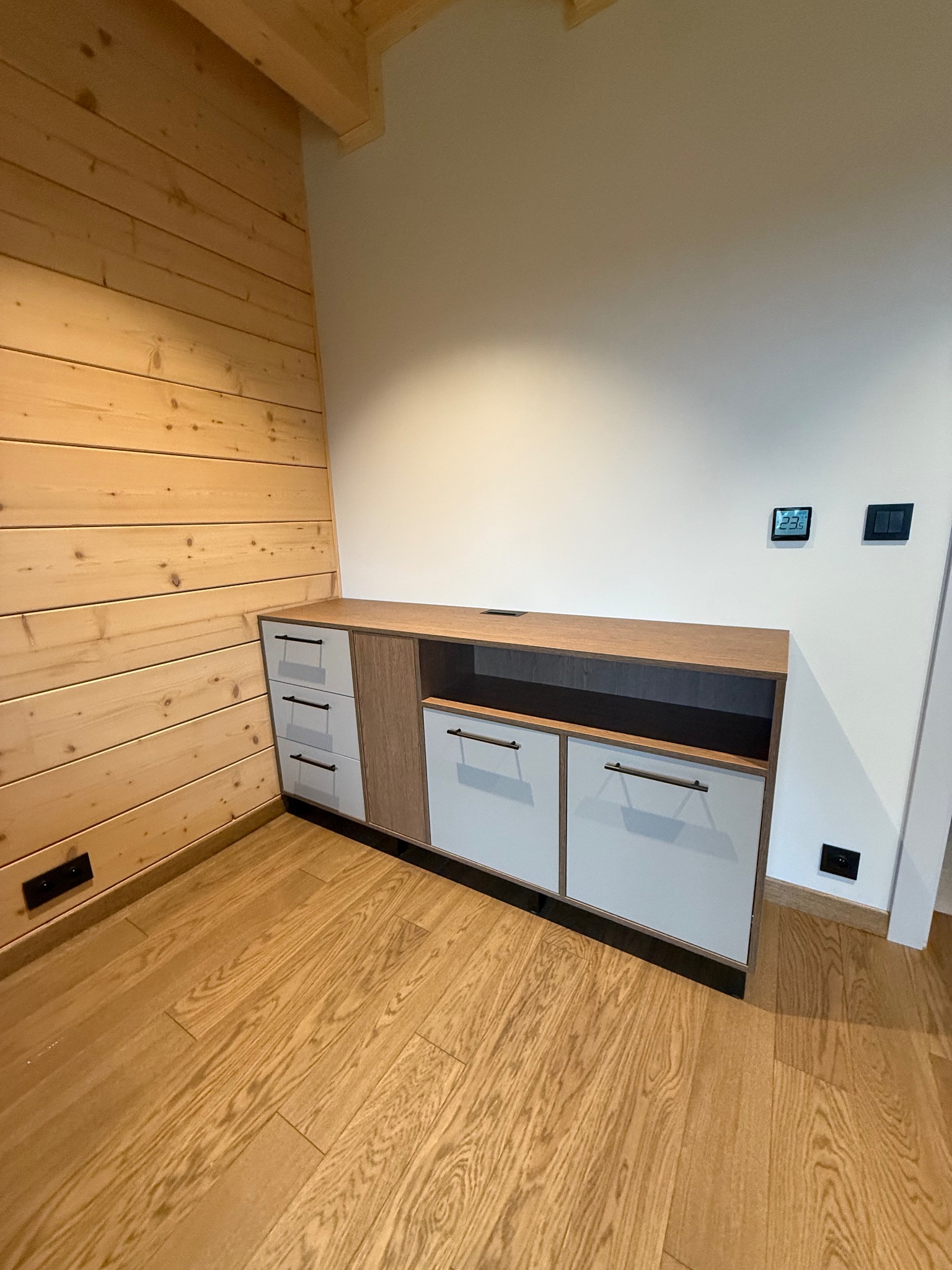 Nowoczesna komoda z szufladami i szafkami w jasnych kolorach, idealnie wpasowana w drewniane wnętrze. Realizacja z Poznania.