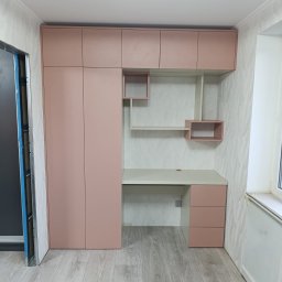 VitiukMeble - Różowa zabudowa meblowa z szafą i biurkiem w pokoju. Szafki wiszące nad blatem biurka z półkami. Nowoczesny design, jasne wnętrze, panele podłogowe.