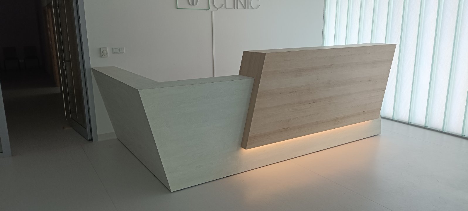 Nowoczesna lada recepcyjna z podświetleniem LED, wykonana z drewna i betonu architektonicznego, na tle ściany z lamelami w jasnym wnętrzu kliniki.