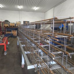 ETER STAL Adrian Pasiniewicz - Gotowa klatka zbrojeniowa na metalowym wózku w hali produkcyjnej. Widoczne elementy konstrukcyjne i spawane łączenia. W tle maszyny i materiały budowlane.