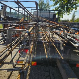 ETER STAL Adrian Pasiniewicz - Transport zbrojenia na przyczepie w słoneczny dzień. Widoczne elementy konstrukcji i tablica rejestracyjna pojazdu. Zastosowanie stali żebrowanej.