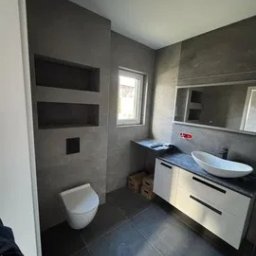 DECOR SYSTEM DESIGN SPÓŁKA Z OGRANICZONĄ ODPOWIEDZIALNOŚCIĄ - Nowoczesna łazienka w szarościach: podwieszana toaleta, umywalka nablatowa, szafka z białymi frontami, wnęki w ścianie. Minimalistyczny design, ciemna podłoga.