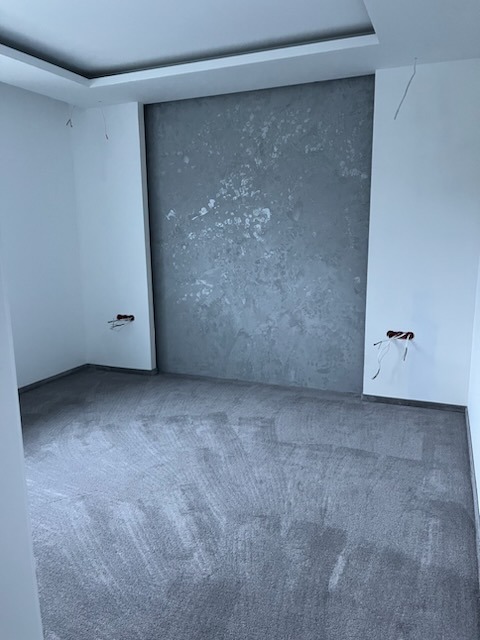 Pokój po szpachlowaniu: szara ściana z efektem dekoracyjnym, przygotowana podłoga, wystające kable elektryczne. Widok z niskiego kąta.