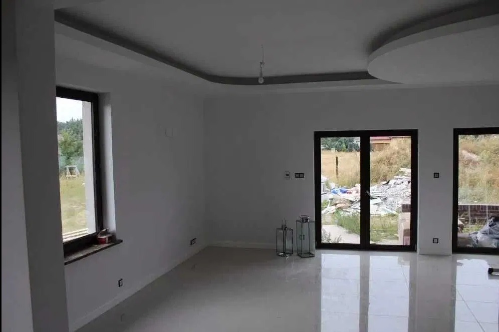 Jasne, przestronne wnętrze po remoncie: białe ściany, błyszcząca podłoga, duże okna z widokiem na zieleń. Sufit z dekoracyjnym oświetleniem. Minimalistyczny design.