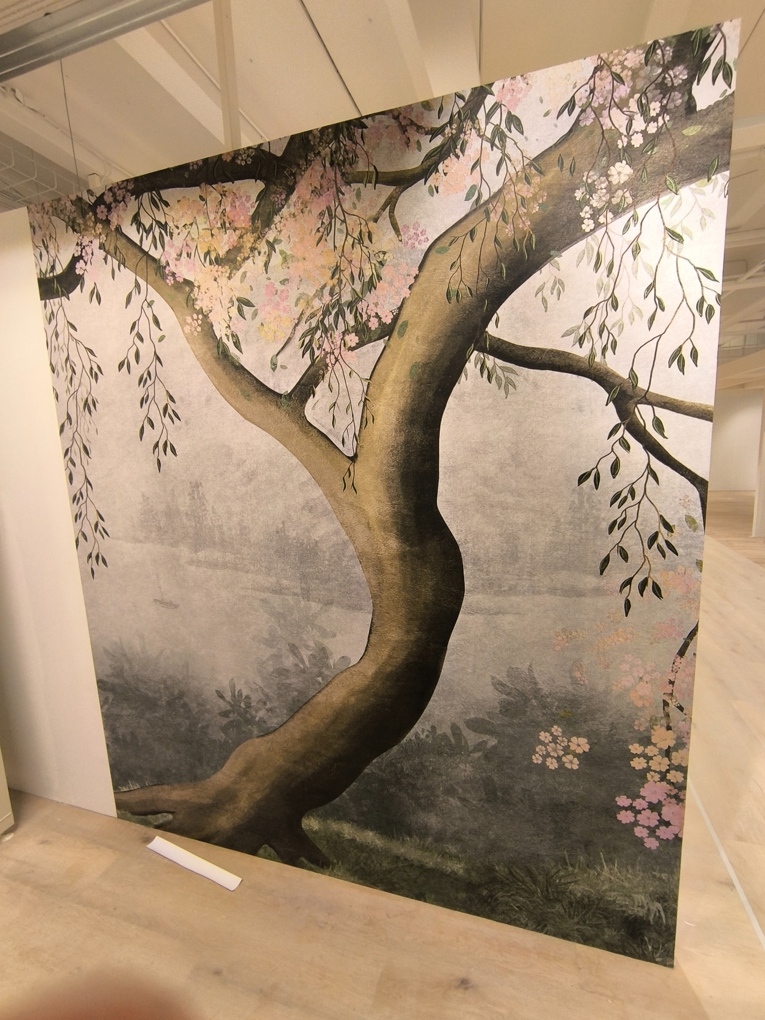 Ściana z fototapetą przedstawiającą drzewo wiśni z kwiatami, widok z dołu, jasne drewniane podłogi, minimalistyczne wnętrze, delikatne kolory.