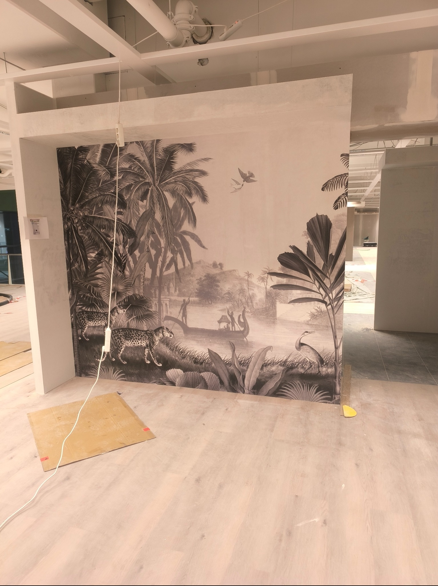 Ściana z fototapetą w stylu retro z motywem dżungli, widoczna w trakcie prac wykończeniowych. Na podłodze leży karton zabezpieczający.