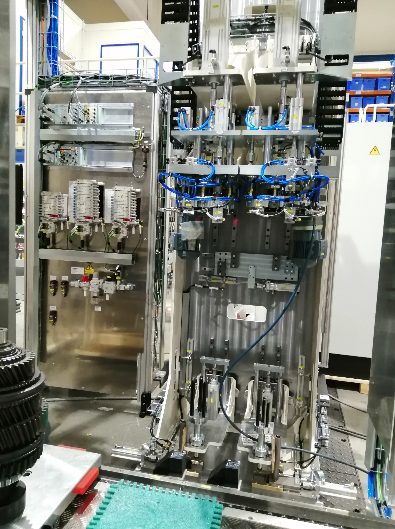 Otwarta szafa sterownicza z widocznymi elementami elektrycznymi, pneumatycznymi i hydraulicznymi. Skomplikowany układ przewodów i komponentów. Widoczne ostrzeżenie o napięciu.