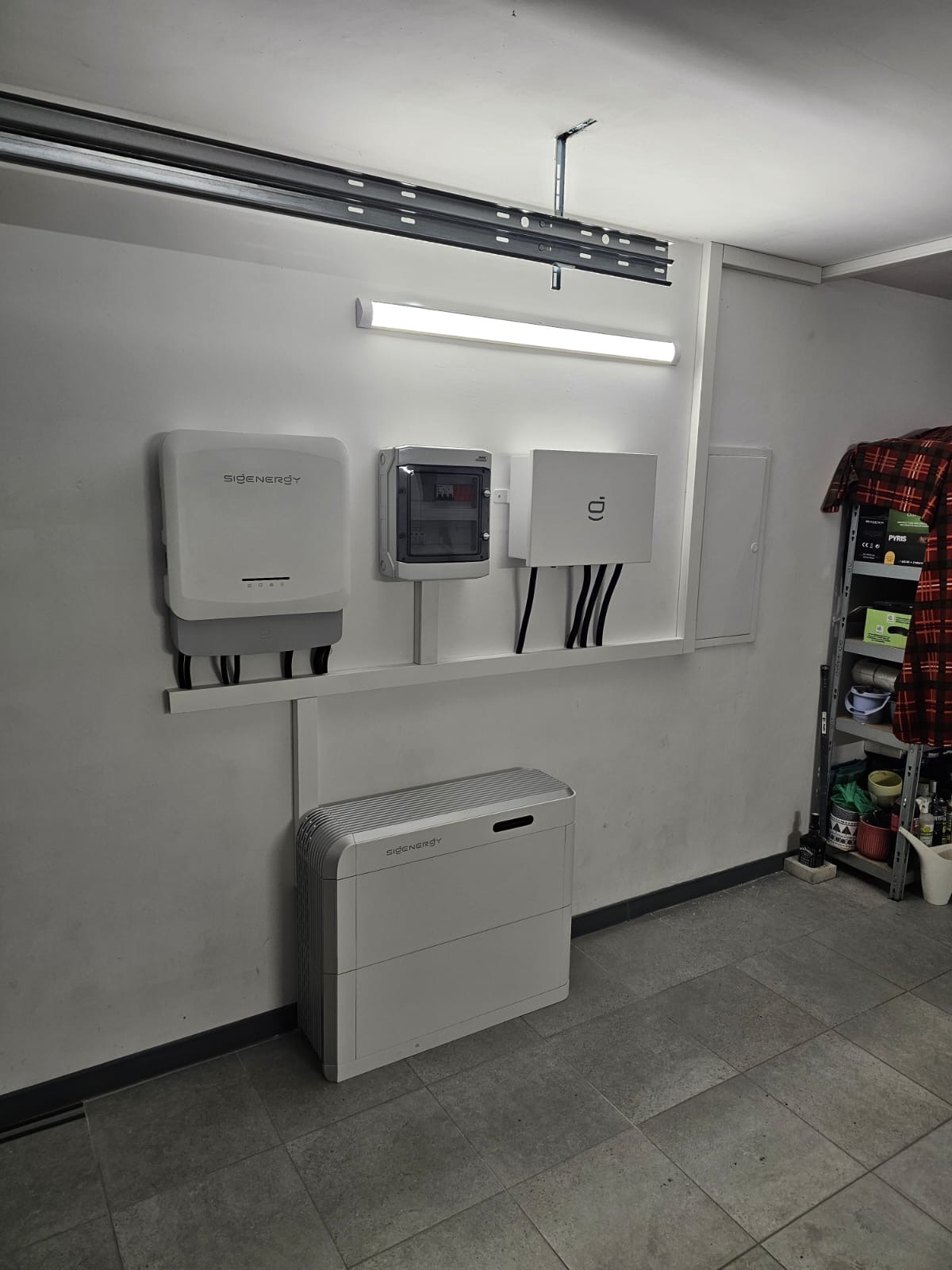 Instalacja magazynu energii Sigen w garażu w Złoczewie. Widoczny inwerter, rozdzielnica i bateria. Minimalistyczny design, szara podłoga z płytek.