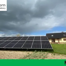 Instalacja paneli na ziemi przed domem jednorodzinnym, widoczne burzowe chmury i ogródek warzywny