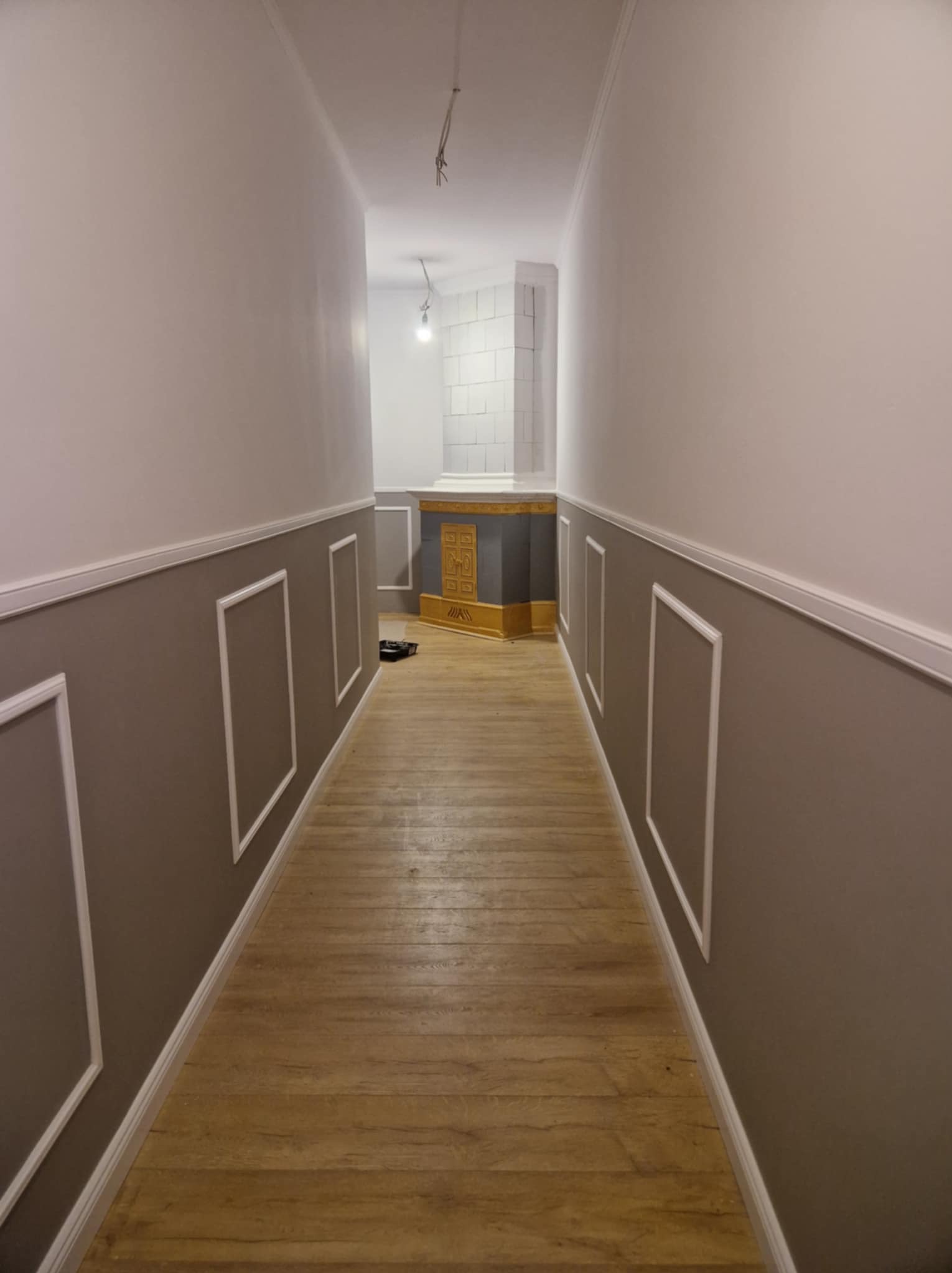 Korytarz po malowaniu ścian w dwóch odcieniach szarości, z dekoracyjnymi białymi listwami. Na końcu widoczny fragment pieca kaflowego i białe płytki.