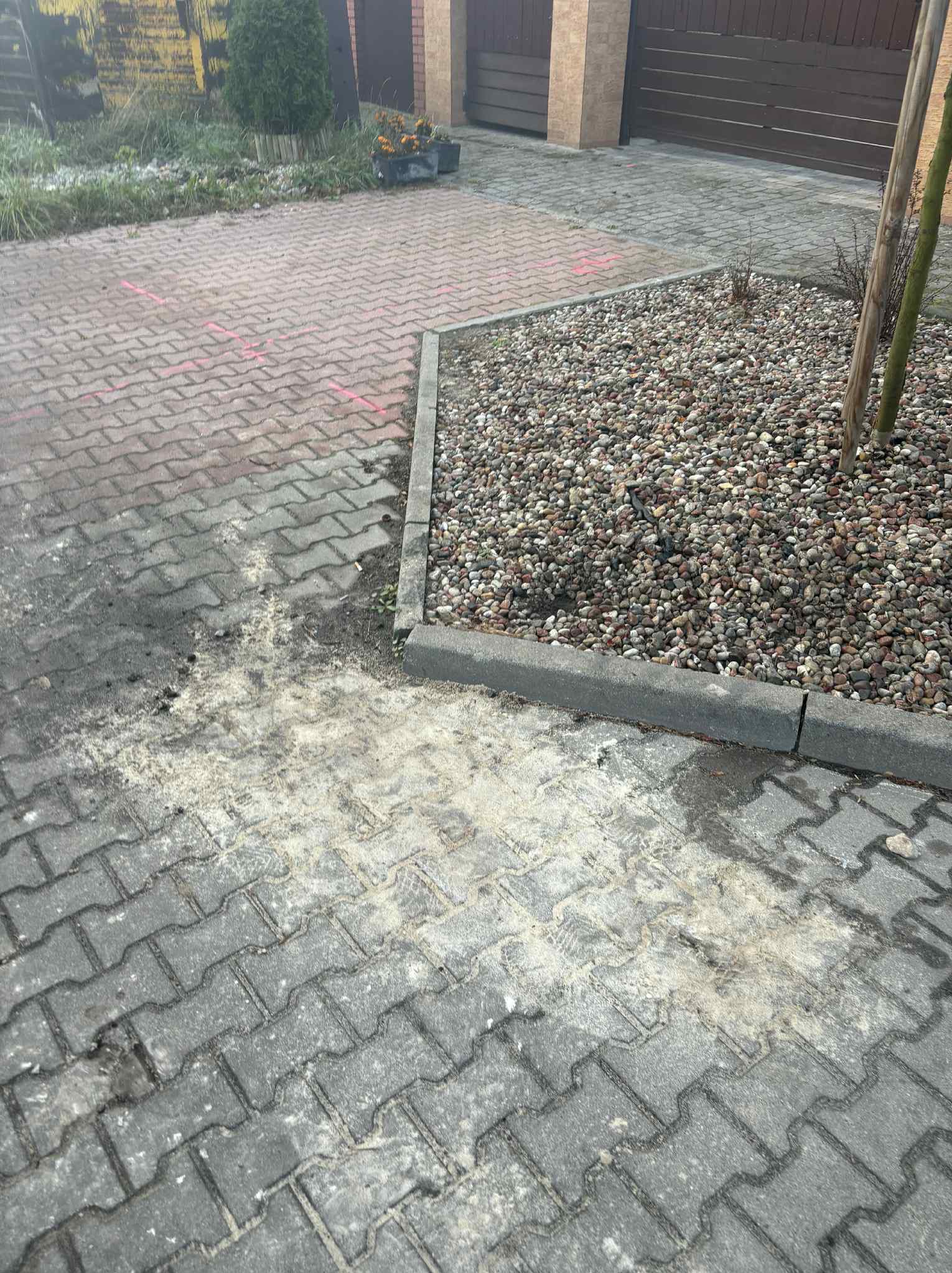 Fragment posesji z kostką brukową w dwóch odcieniach szarości i czerwieni, obok rabata z kamieniami. Widoczne ślady po czyszczeniu kostki. Ujęcie z góry.