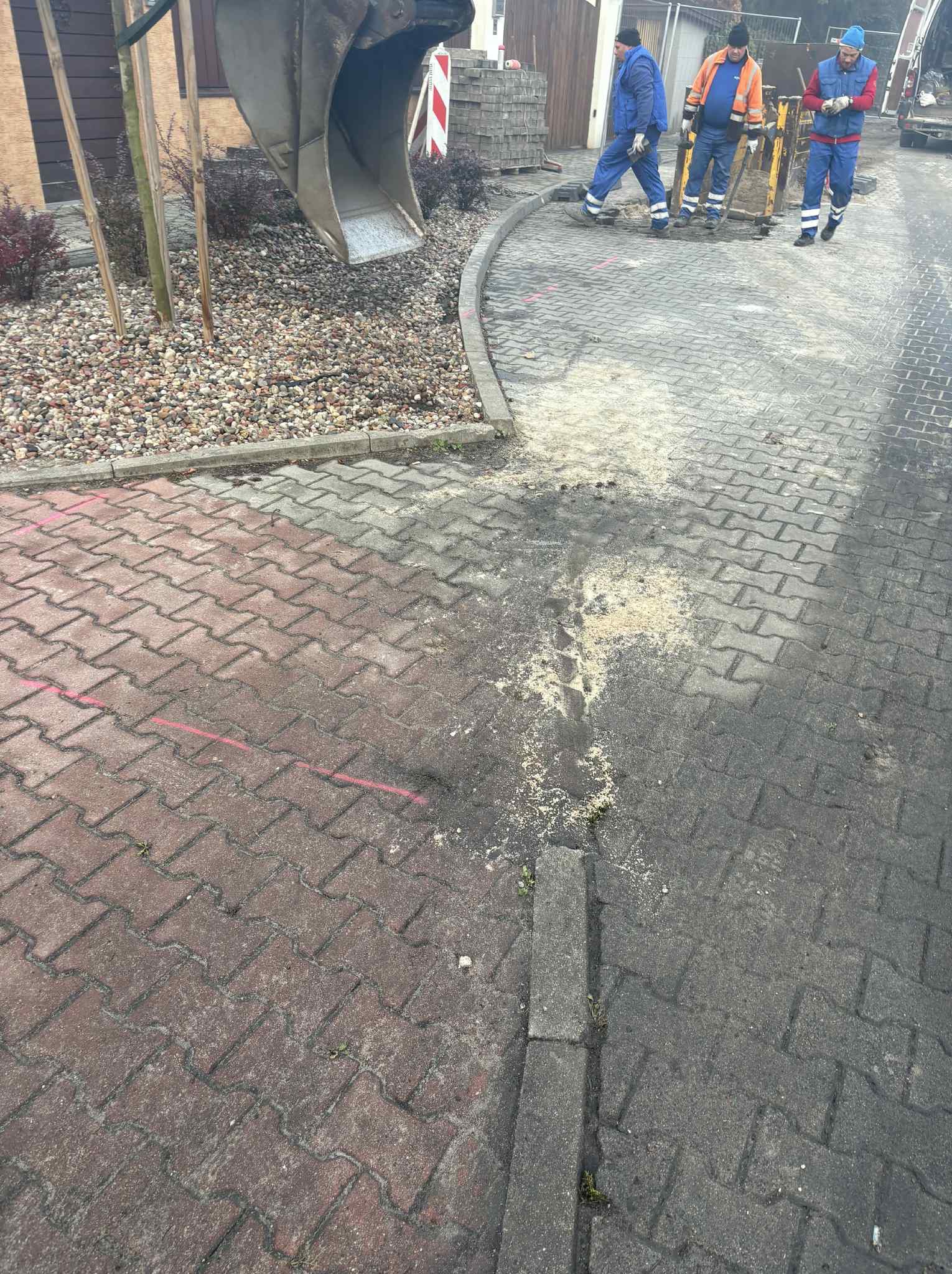 Prace brukarskie w toku: ekipa robotników wyrównuje teren pod kostkę brukową. Widoczny fragment ułożonej kostki, piasek i maszyny budowlane. Ujęcie z góry.