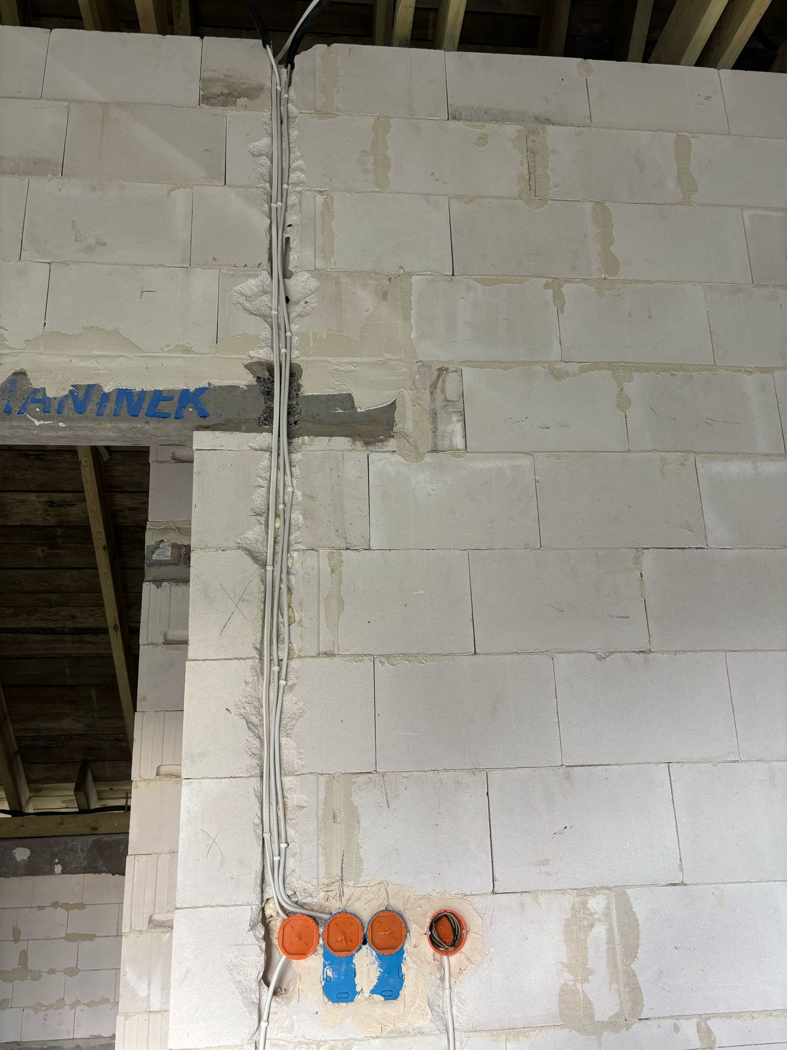 Ściana z betonu komórkowego z widocznymi przewodami elektrycznymi w peszlach i puszkami instalacyjnymi. Etap prac przed tynkowaniem. Widoczne oznaczenia na ścianie.