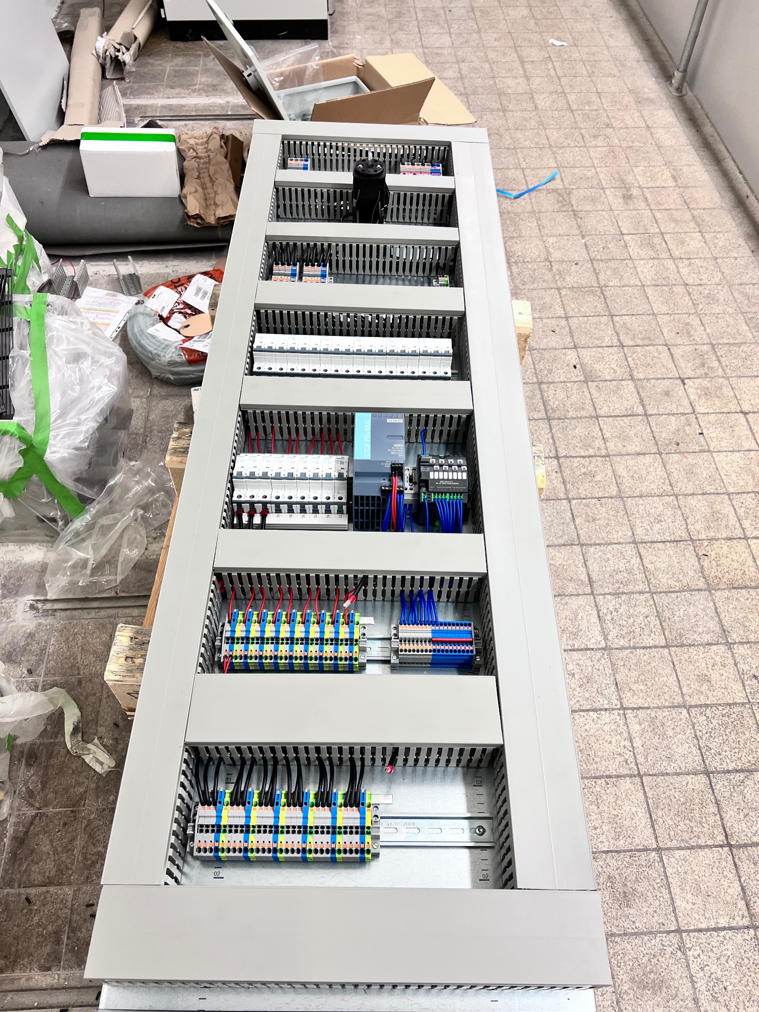 Rozdzielnica elektryczna z widocznymi bezpiecznikami, przewodami i złączkami, zamontowana w szarej obudowie. Widok z góry, ukazujący szczegóły instalacji.