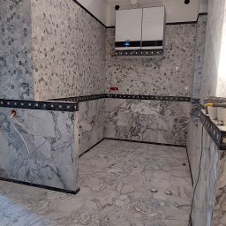 Oleh Mytulynskyi - Wykończona łazienka z marmurowymi płytkami na ścianach i podłodze, z zamontowanym piecem gazowym. Widoczne narzędzia glazurnicze.