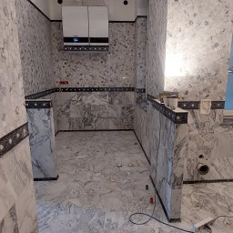 Oleh Mytulynskyi - Wykończona łazienka z marmurowymi płytkami heksagonalnymi na ścianach i podłodze. Widoczny piec dwufunkcyjny. Dekoracyjne listwy. Częściowo widoczne narzędzia.