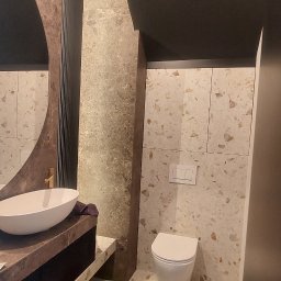 Oleh Mytulynskyi - Wykończona łazienka z umywalką na blacie, toaletą i płytkami imitującymi lastryko. Widoczne akcesoria i narzędzia sugerują świeżo zakończone prace.