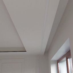 Oleh Mytulynskyi - Białe wnętrze w trakcie wykończenia: sufit podwieszany z oświetleniem, ściana z gniazdkami i instalacją elektryczną, okno z widocznymi żaluzjami.