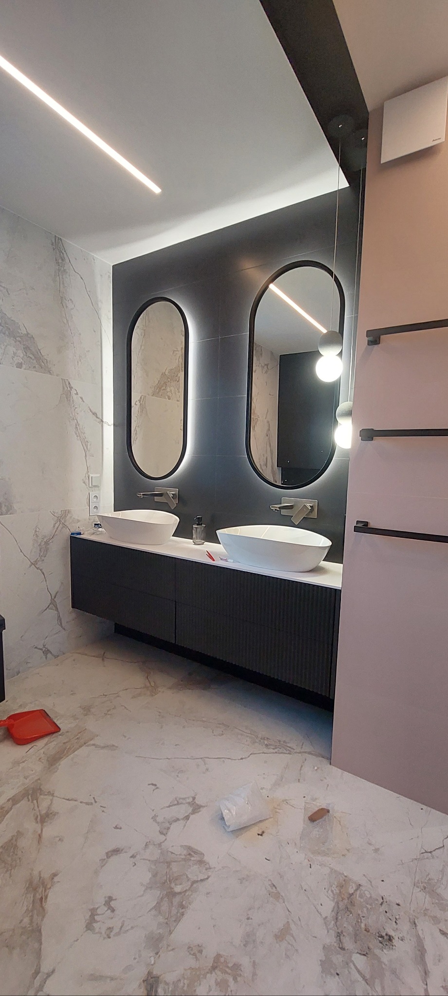 Nowoczesna łazienka z dwoma owalnymi lustrami z podświetleniem LED, umywalkami nablatowymi i marmurową posadzką. Minimalistyczny design, czarne akcenty i subtelne oświetlenie.