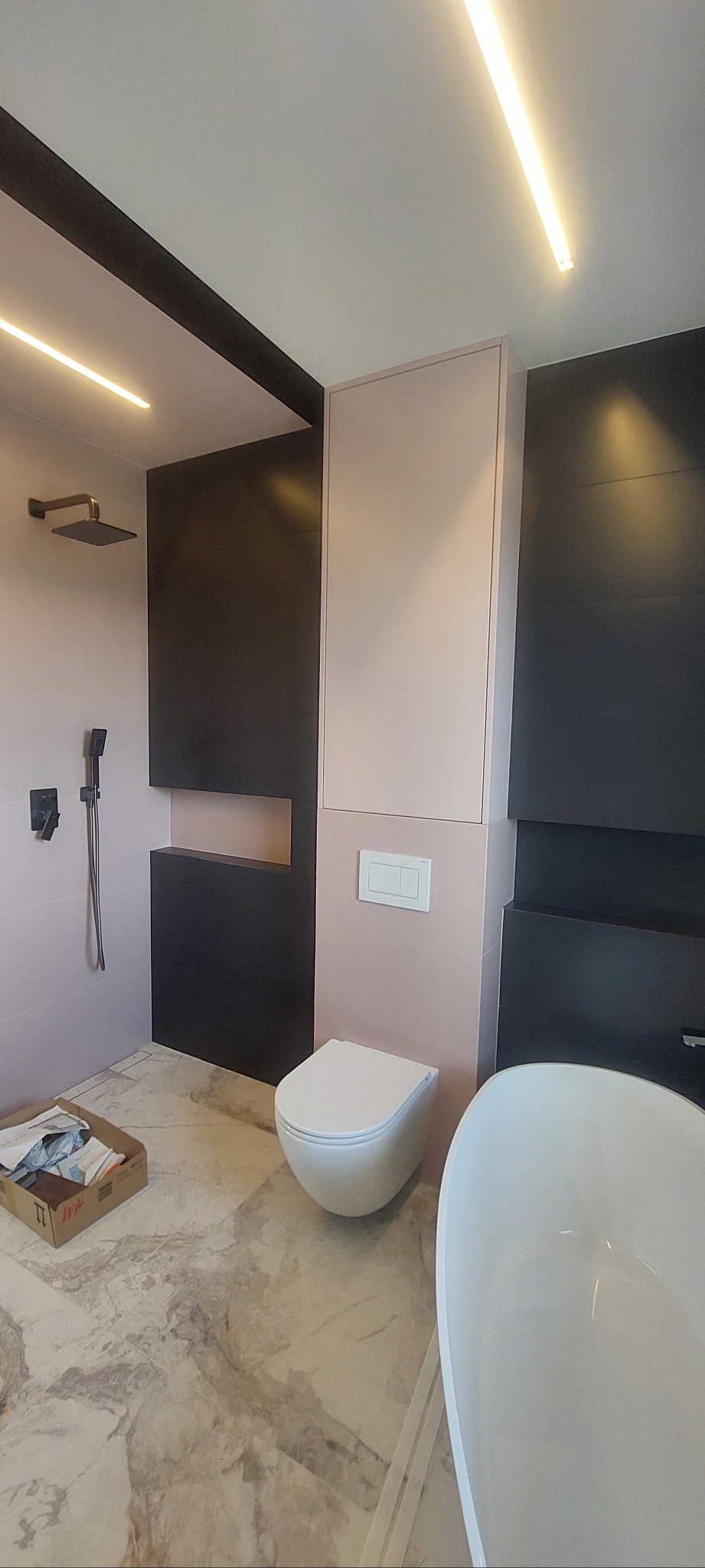 Nowoczesna łazienka z elementami czerni i pudrowego różu: wisząca toaleta, wanna, kabina prysznicowa typu walk-in, marmurowe płytki podłogowe i oświetlenie LED.