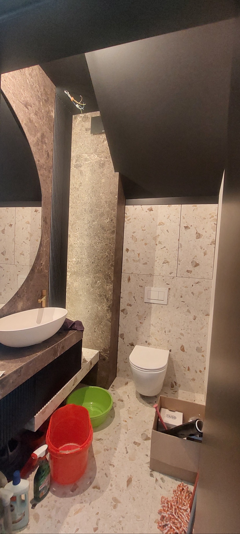 Wykończona łazienka z umywalką na blacie, toaletą i płytkami imitującymi lastryko. Widoczne akcesoria i narzędzia sugerują świeżo zakończone prace.