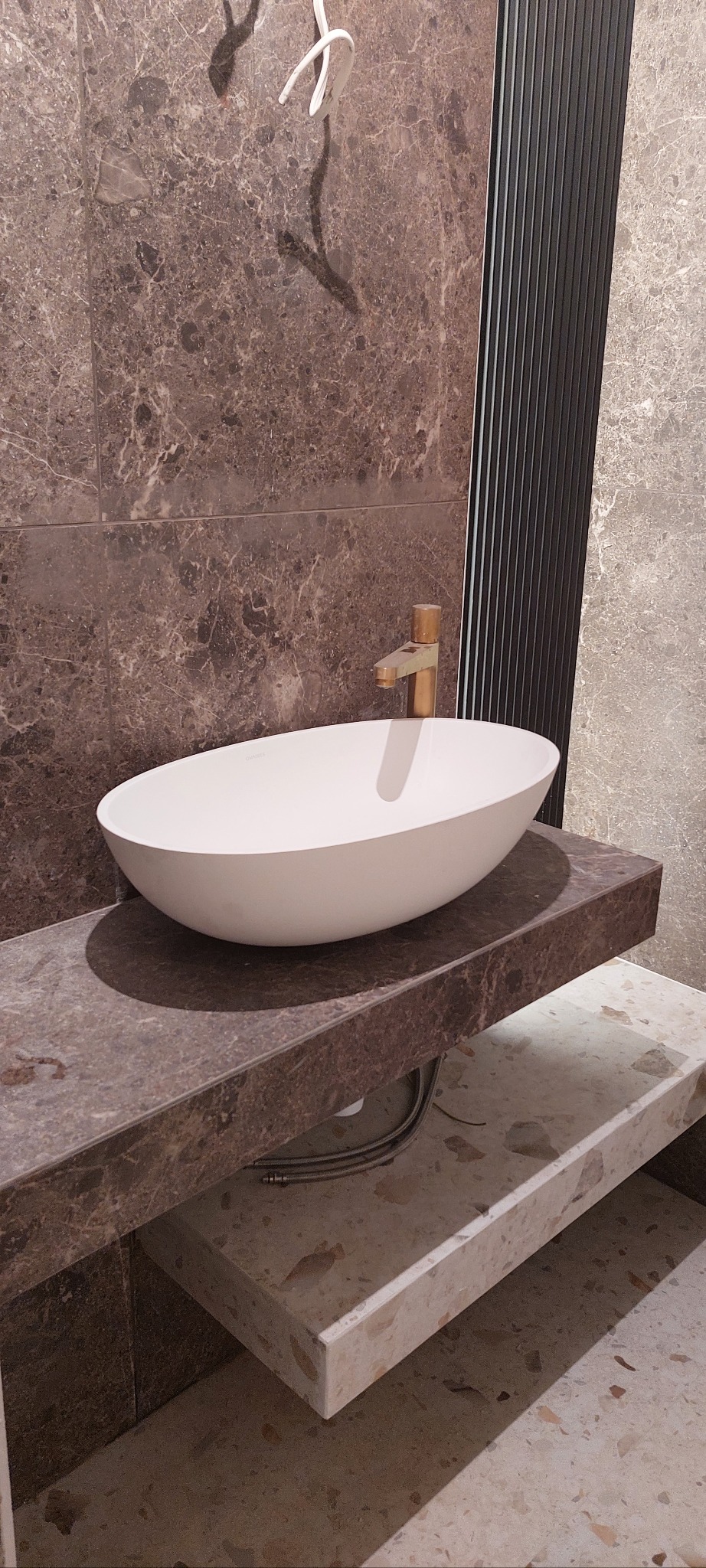 Nowoczesna łazienka: owalna umywalka nablatowa z baterią w kolorze złota, marmurowe płytki na ścianie i blacie, minimalistyczny design.