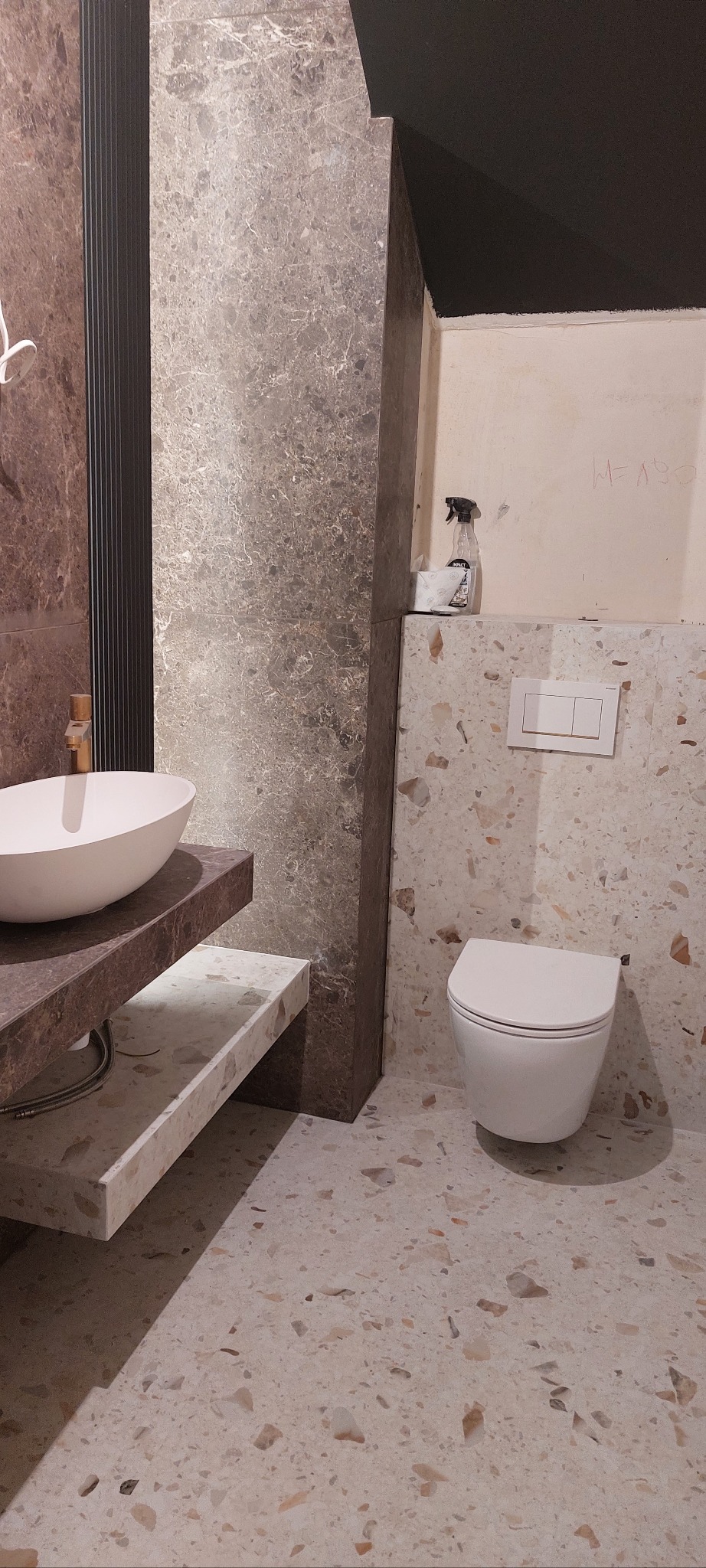 Nowoczesna łazienka z umywalką nablatową, marmurowymi płytkami i podwieszaną toaletą. Widoczne detale wykończenia i armatura w kolorze złota.