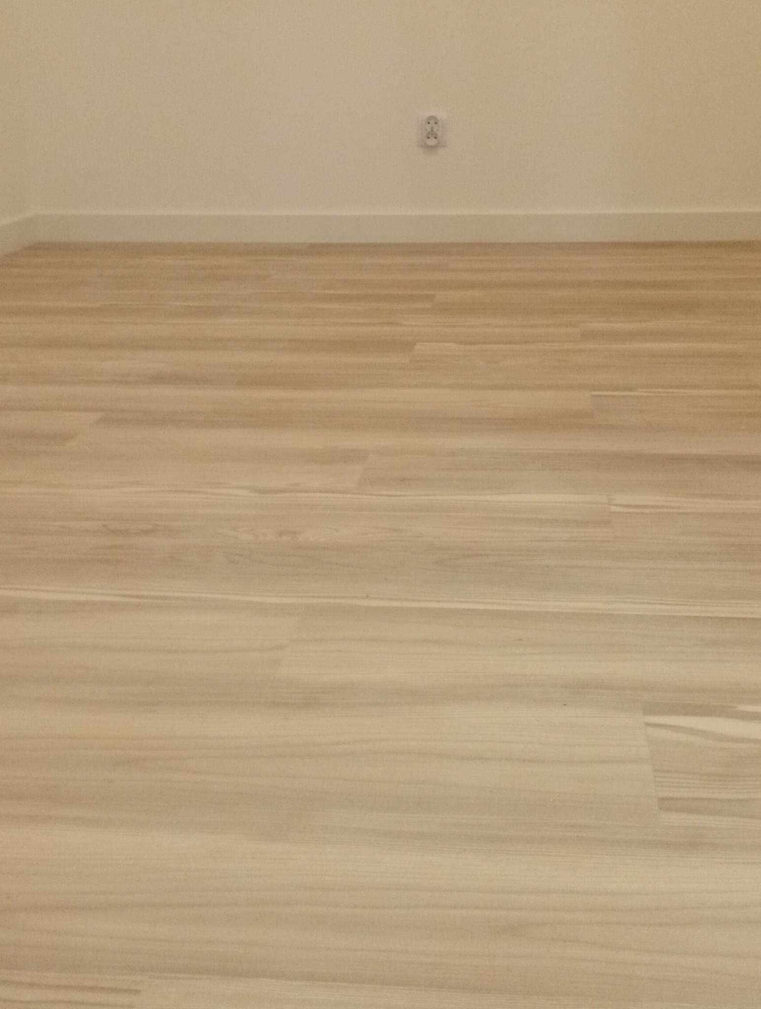 Jasna, drewnopodobna podłoga po remoncie, świeżo ułożona, z widoczną listwą przypodłogową i gniazdkiem elektrycznym na ścianie. Minimalistyczne wykończenie wnętrza.