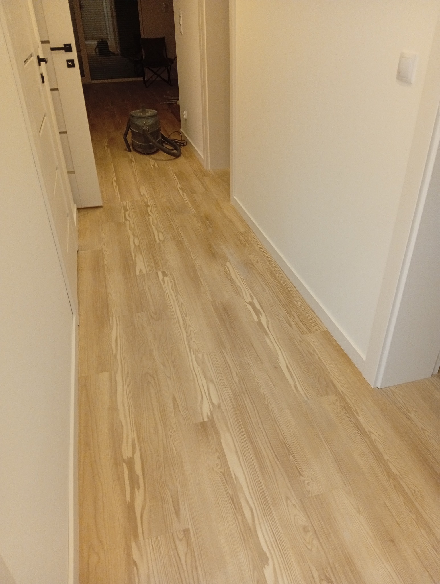 Jasna, drewniana podłoga po renowacji w korytarzu, widoczny odkurzacz przemysłowy. Świeżo pomalowane ściany i listwy przypodłogowe.