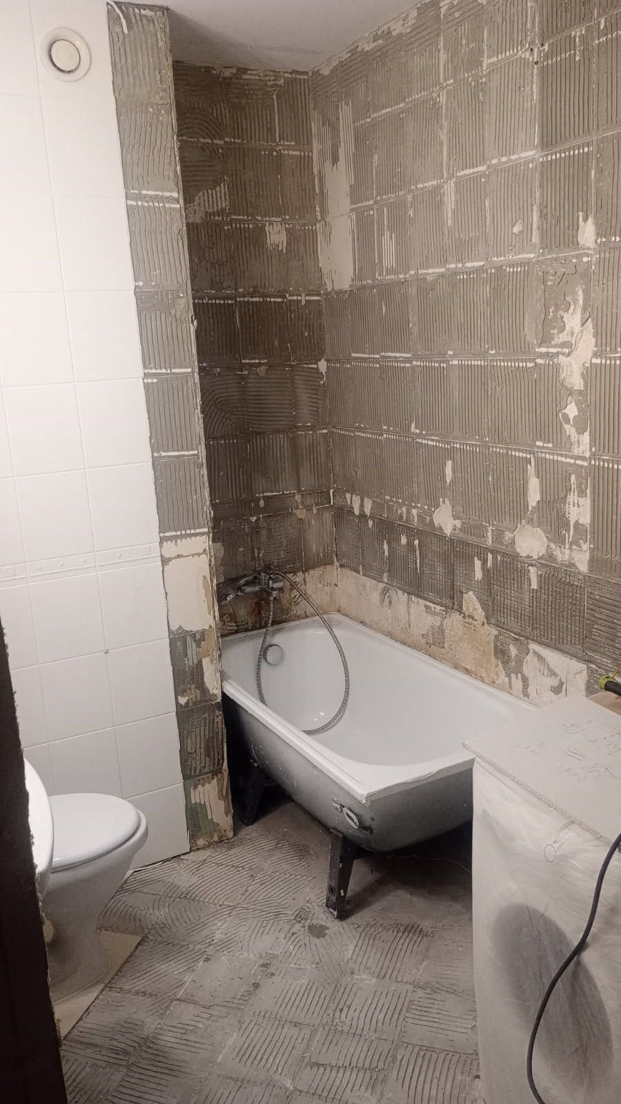 Demontaż płytek w łazience przed remontem. Widoczna wanna, toaleta i ściany z resztkami kleju po usuniętych płytkach. Przygotowanie do dalszych prac remontowych.