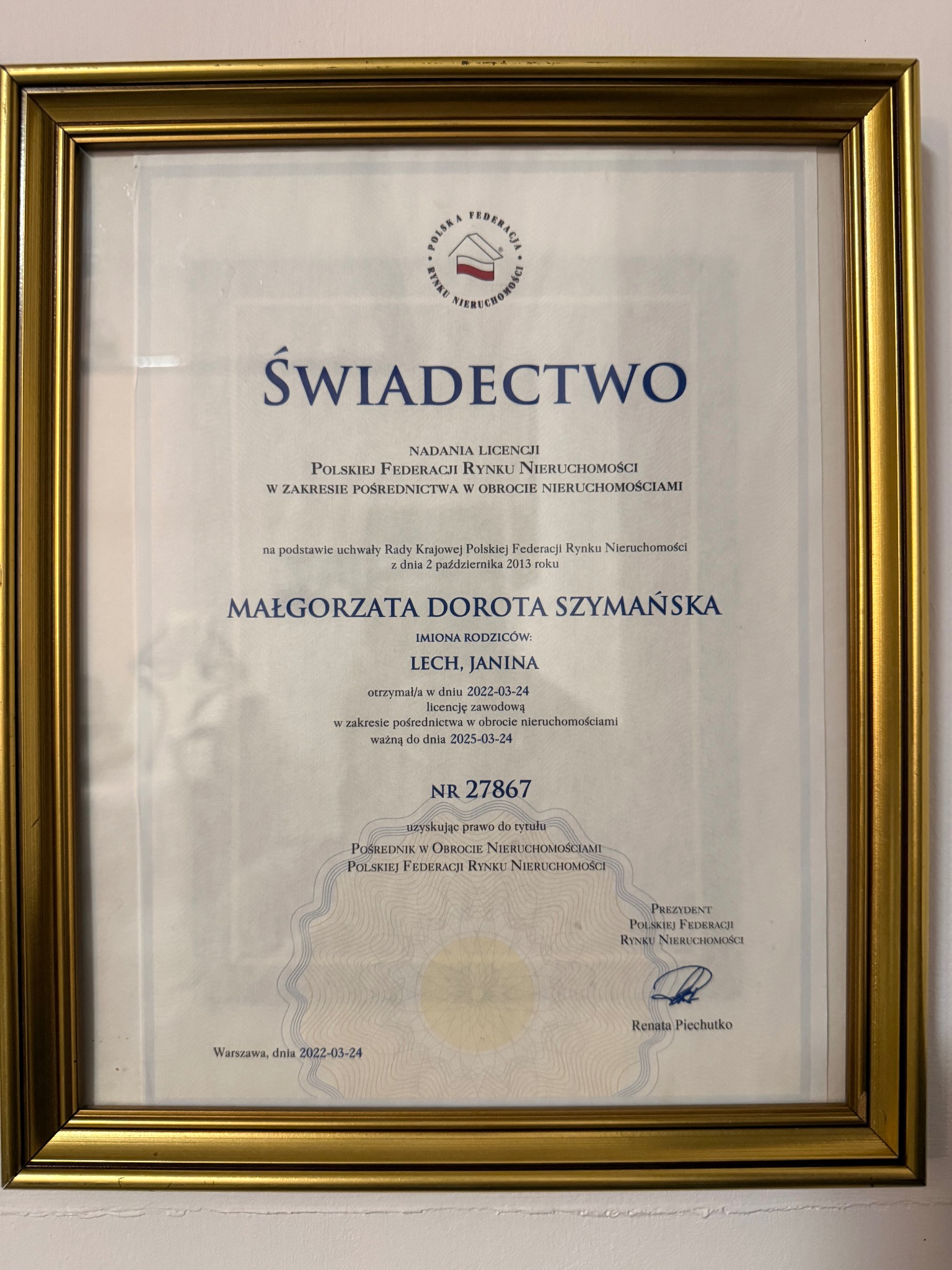 Świadectwo nadania licencji pośrednika w obrocie nieruchomościami Małgorzaty Doroty Szymańskiej, wydane przez Polską Federację Rynku Nieruchomości, w złotej ramie.