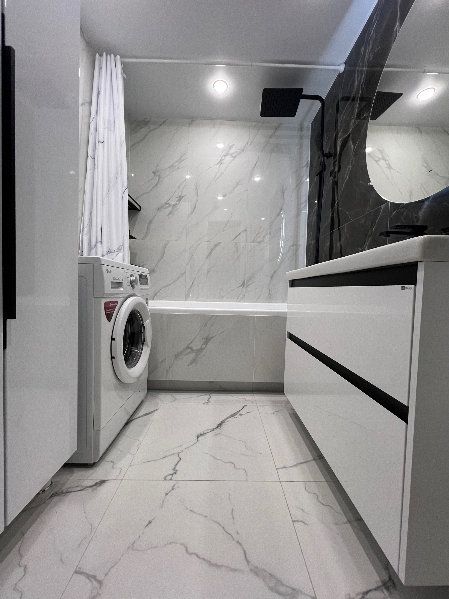 Nowoczesna łazienka z marmurowymi płytkami, białą armaturą i pralką. Minimalistyczny design z czarnymi akcentami. Ujęcie z perspektywy podłogi.