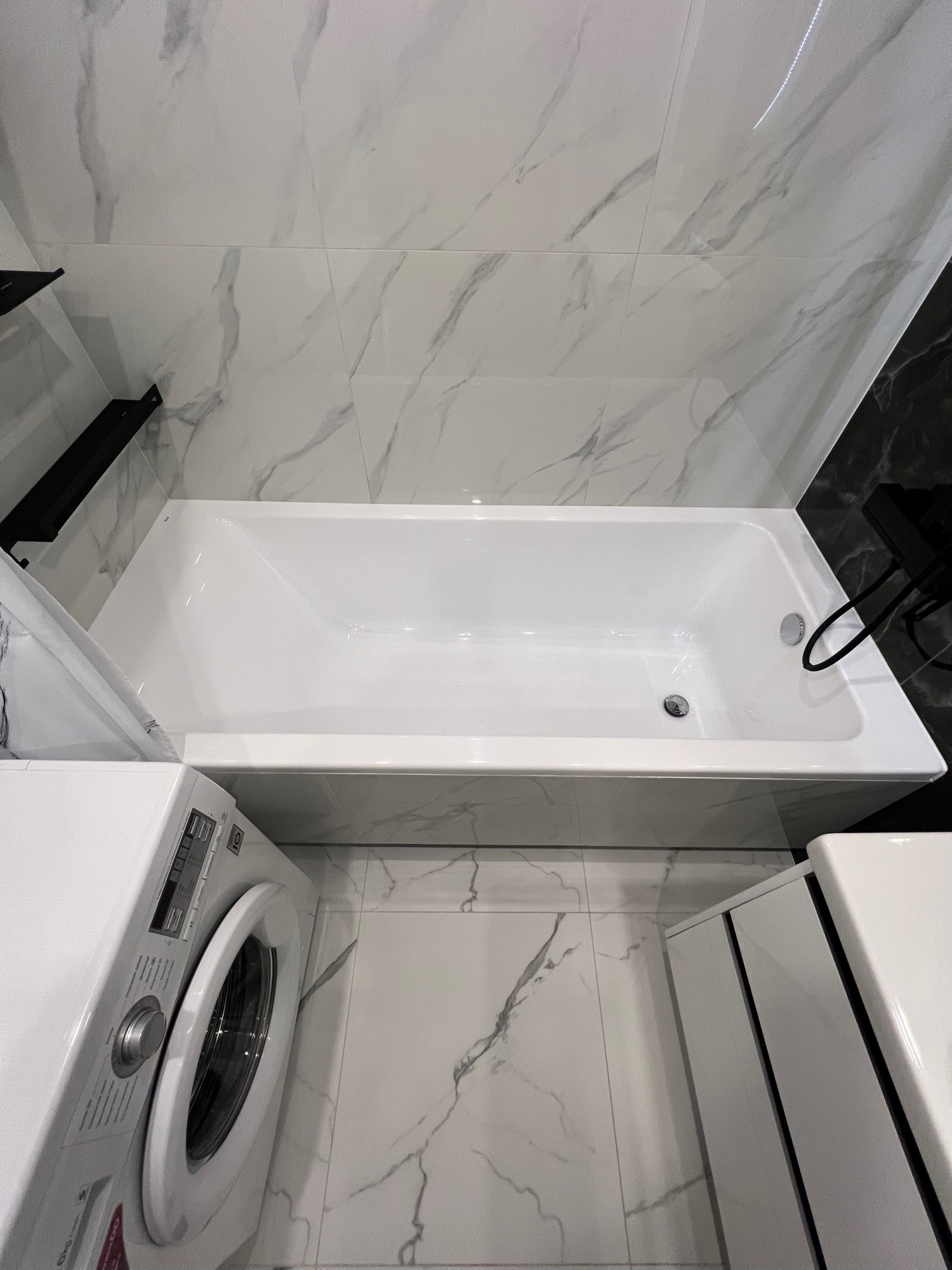 Nowoczesna łazienka z białą wanną, pralką i marmurowymi płytkami. Ujęcie z góry podkreśla minimalistyczny design i czystość wykończenia.