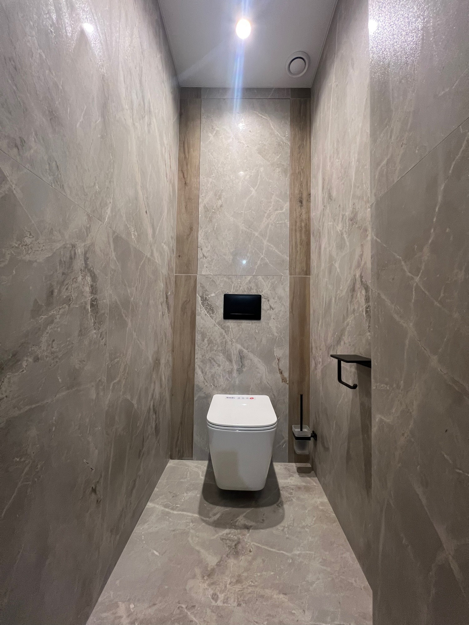 Elegancka toaleta w odcieniach szarości z marmurowymi płytkami, podświetlona punktowym światłem. Minimalistyczny design z akcentami drewna.