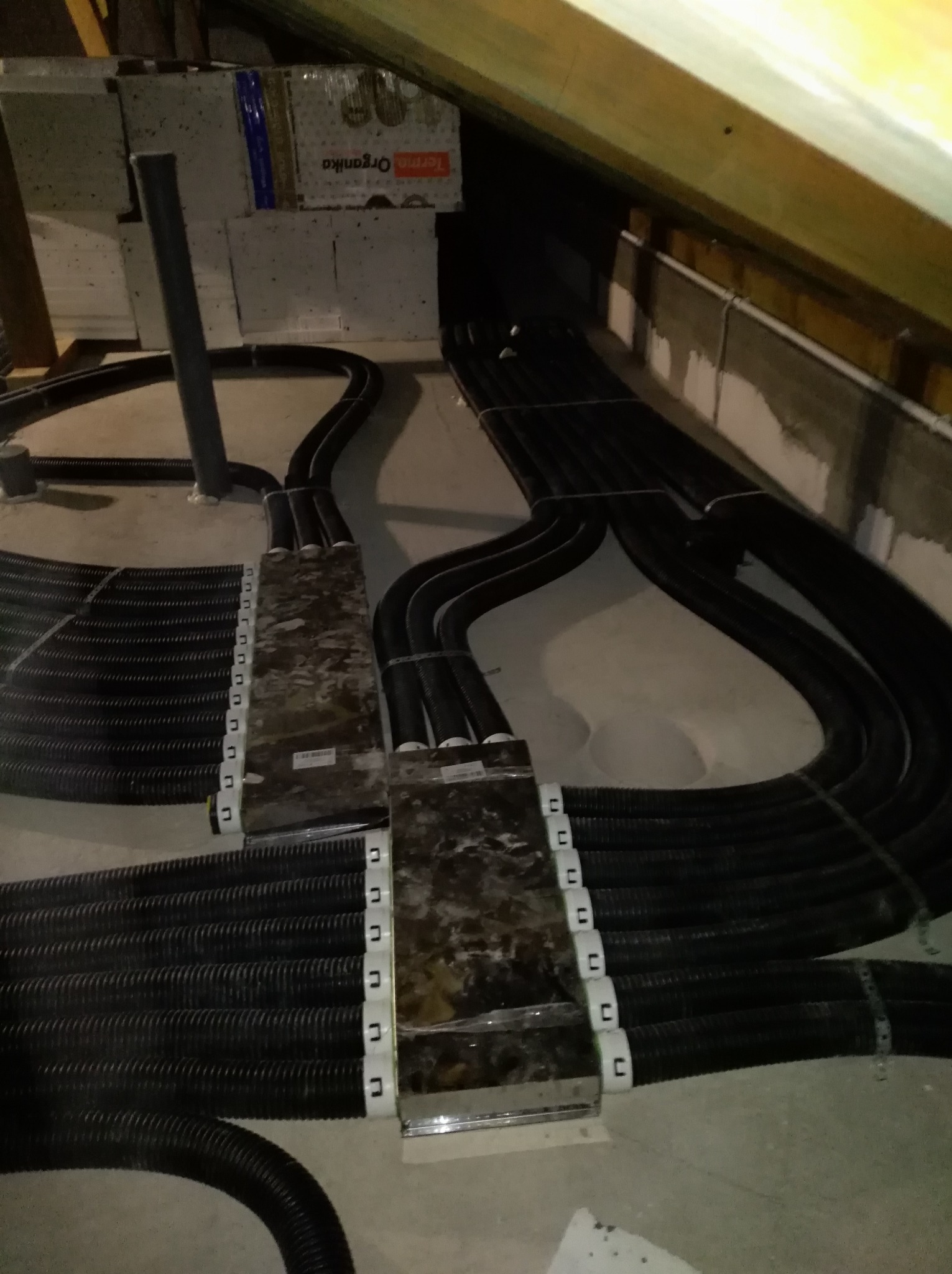 Rozłożone czarne rury ogrzewania podłogowego w trakcie montażu, widoczne elementy mocujące i izolacja. Ujęcie z góry, w pomieszczeniu ze skosami.