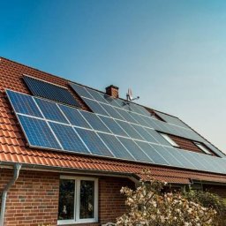 Solidus - Czerwony dach z panelami słonecznymi i kolektorami słonecznymi na ceglanym domu jednorodzinnym w słoneczny dzień. Widok z dołu.