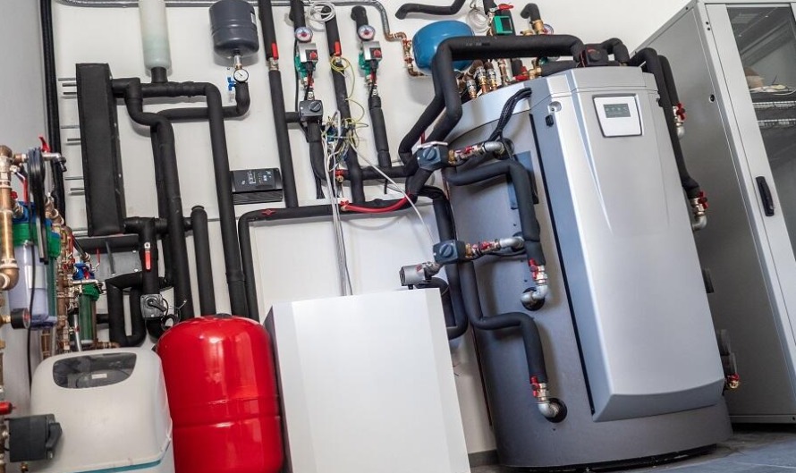 Nowoczesna kotłownia z zaawansowanym systemem rur, zbiorników i urządzeń, w tym srebrny piec z wyświetlaczem, zainstalowana w jasnym pomieszczeniu.