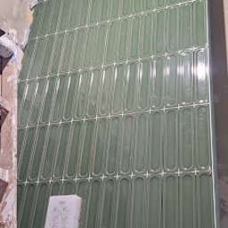 Tomasz Kądziołka usługi budowlane i ogrodnicze - Ściana w trakcie wykańczania z podłużnymi, zielonymi płytkami, widoczne krzyżyki dystansowe i niedokończone fragmenty ściany. Ujęcie z dołu.