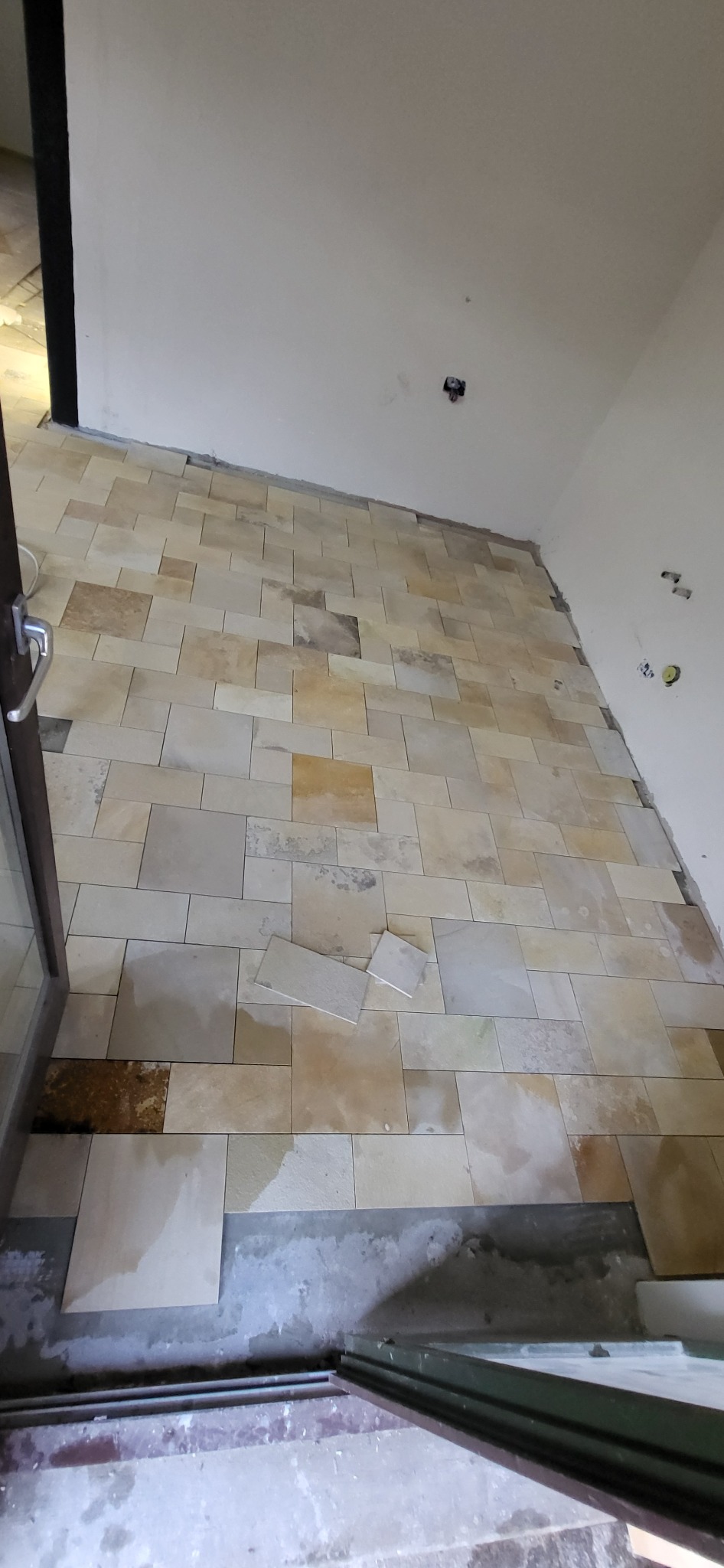 Układanie jasnych, prostokątnych płytek na podłodze w Świdniku. Widoczne niedokończone fragmenty i surowe ściany. Prace glazurnicze w trakcie realizacji.