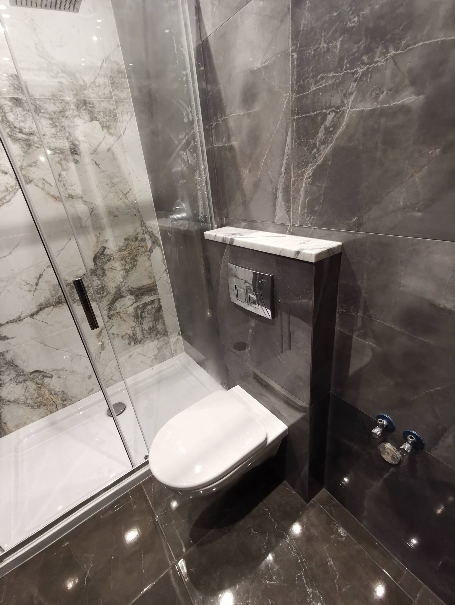 Nowoczesna łazienka z kabiną prysznicową i podwieszaną toaletą. Marmurowe płytki w odcieniach szarości. Bateria podtynkowa. Minimalistyczny design.