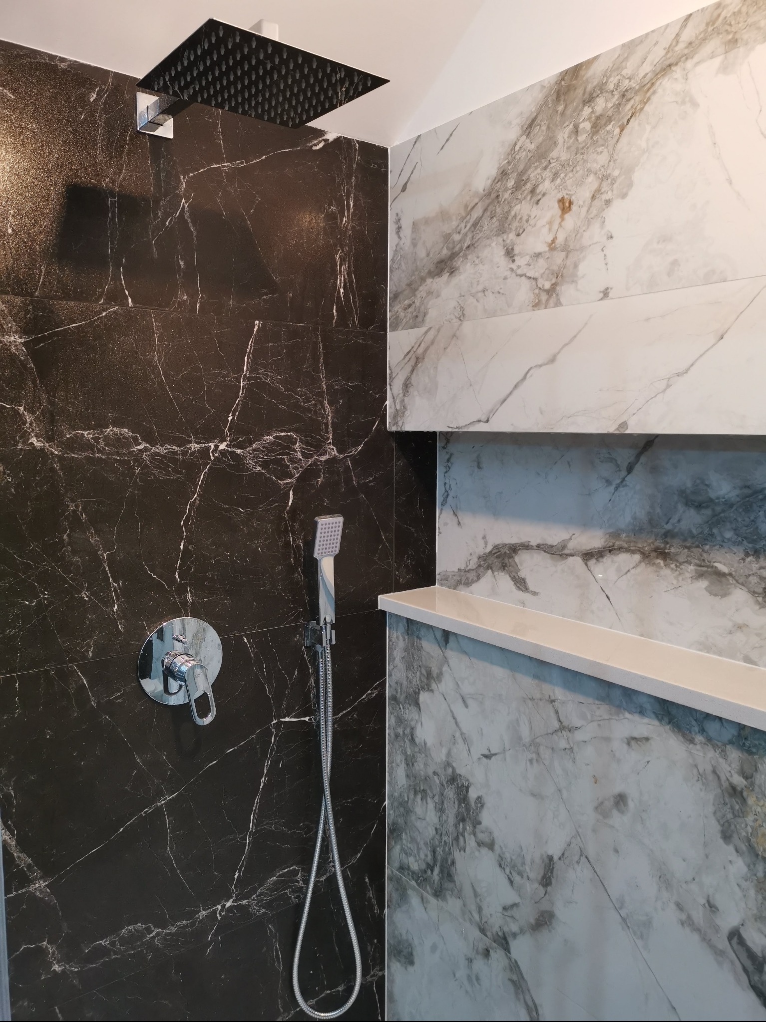 Nowoczesna kabina prysznicowa z czarnymi i białymi płytkami imitującymi marmur, deszczownicą i półkami wnękowymi. Minimalistyczny design.